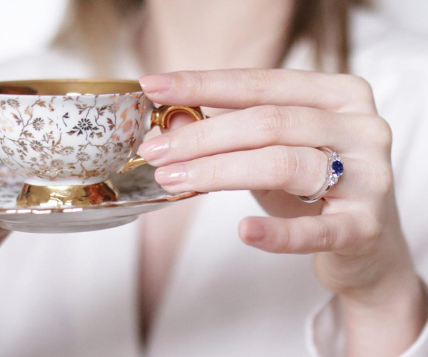 Person drinking tea with sapphire diamond ring on finger