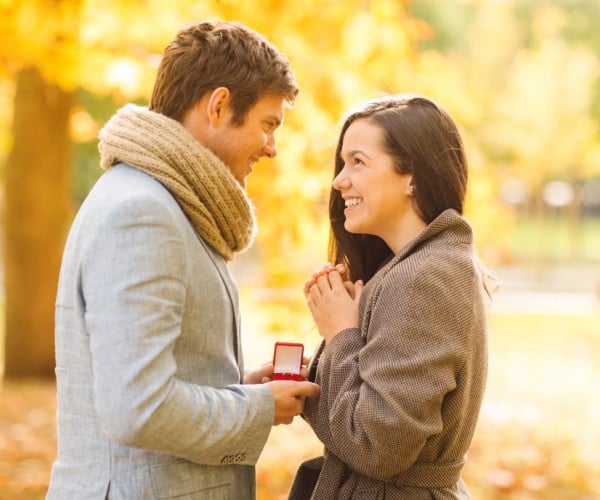 A man proudly presents an engagement ring to his women, celebrating their engagement in a natural setting.