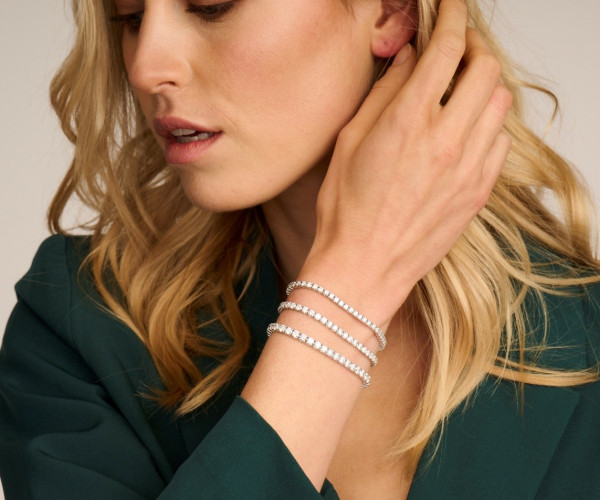 A woman in a green blouse showcases layered gold bracelets on her wrist, highlighting her elegant style