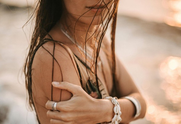 Woman on a beach wearing golden and silver jewellery and sea shell bracelets.