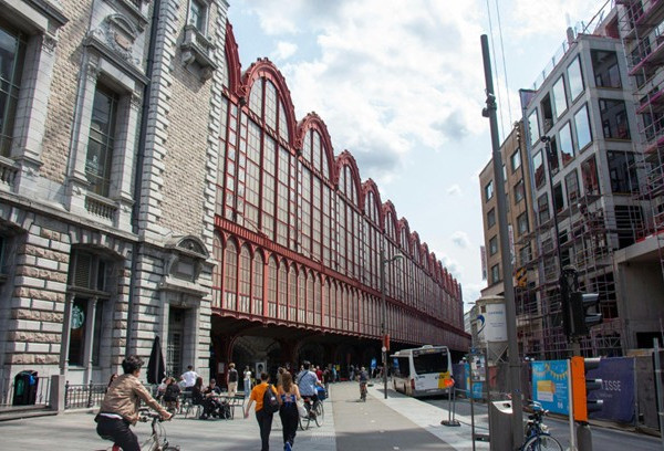 The iconic clock tower of Antwerp Central Station looms over a lively crowd in the Diamond District, embodying the city's rich architectural charm and energy.
