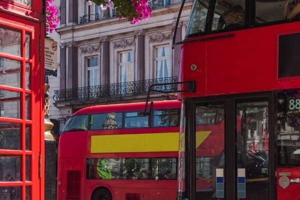 A scenic photograph of a London street with the iconic red telephone cabin and the red tourist buses picturing the busy time of day.