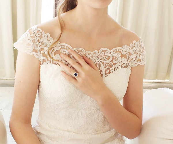 a woman in her wedding dress with her left hand on her chest. Her sapphire entourage engagement ring is showing