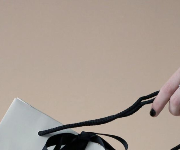 hand of woman wearing cuff bracelet with wavy design holding white bag with black ribbon