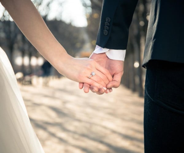 Una coppia che si tiene per mano in un parco, mostrando il proprio amore e il fascino delle superstizioni legate alle fedi nuziali che li circondano.