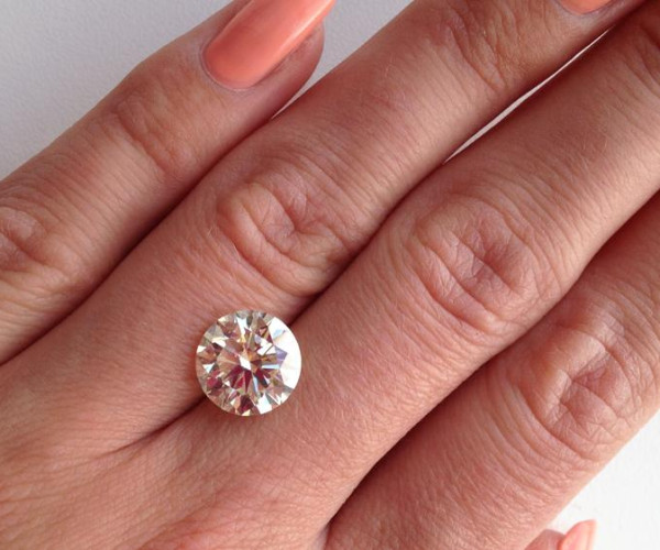 La mano di una donna regge con eleganza un anello di fidanzamento, impreziosito dalla montatura che lo fa apparire più grande e scintillante.