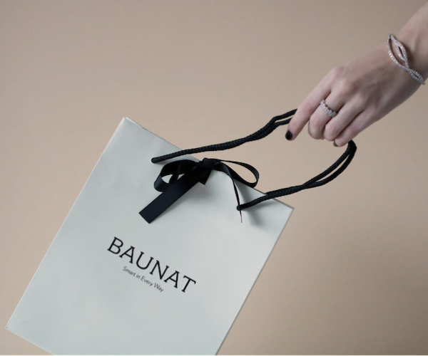 주얼리를 구매한 후 BAUNAT의 흰색 쇼핑백을 들고 있는 사람