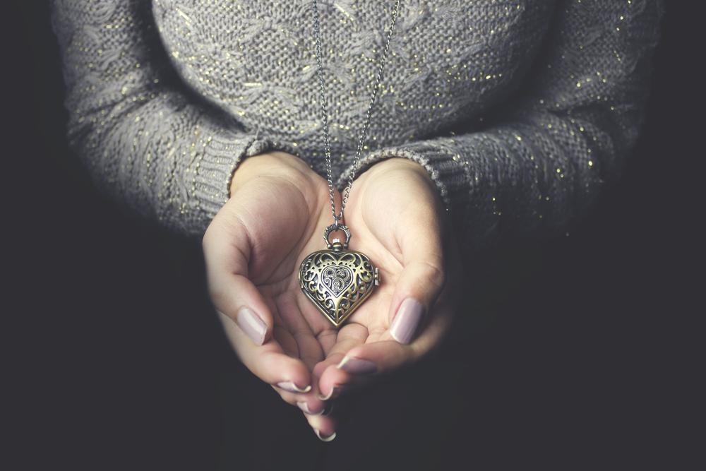 Vrouw met hartvormig medaillon in de hand, een gepersonaliseerd cadeau dat BAUANT op maat maakt.