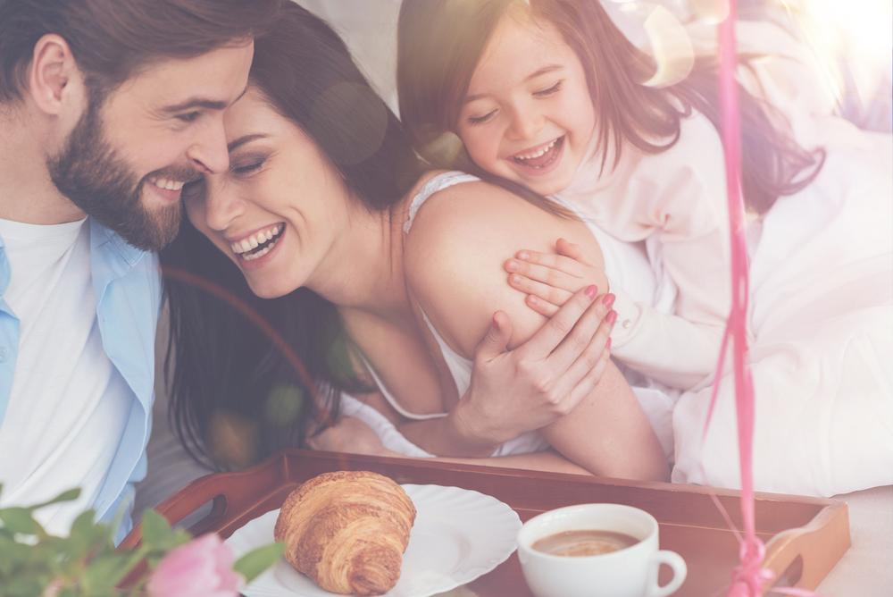 Man en kind brengen moeder ontbijt op bed. BAUNAT geeft tips voor een uniek Moederdag cadeau.