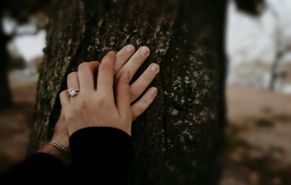 woman holding hand of her husband after he had hidden her engagement ring in a tree trunk
