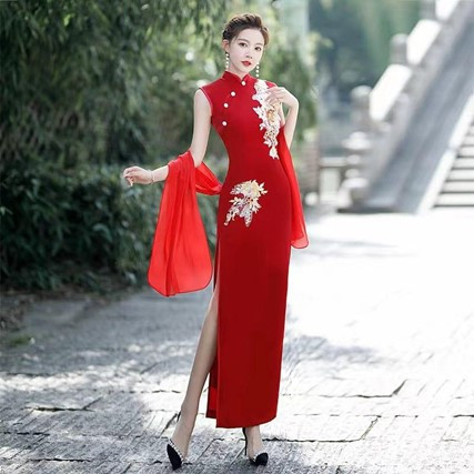 A woman in a red qipao with floral embroidery poses elegantly for a photograph, showcasing traditional Chinese attire