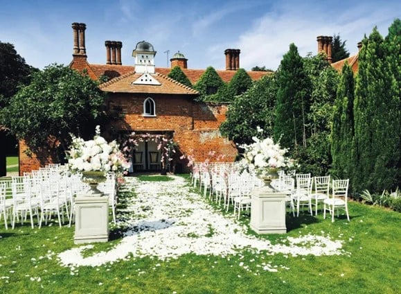 A charming countryside wedding setup in front of a rustic brick building, adorned with flowers and elegant decor, the perfect english wedding venue