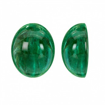 Two oval-shaped cabochon cut emerald stones displayed side by side, showcasing their rich green colour and smooth surface.