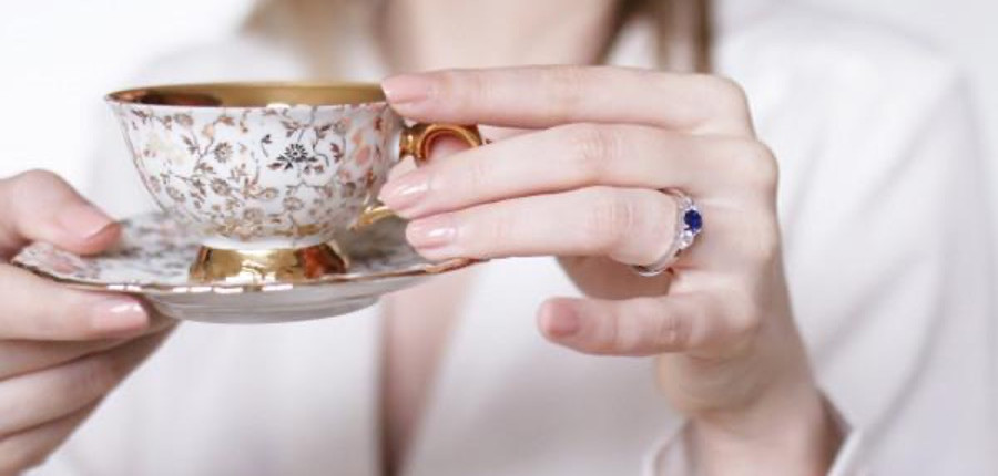 une femme tenant une tasse avec une soucoupe, portant un beau diamant bleu à son doigt