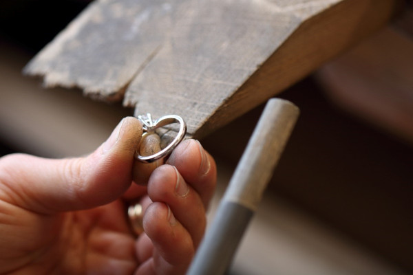 Un gioielliere utilizza uno strumento per lavorare su una macchina, concentrandosi sul ridimensionamento della fascia metallica di un anello.
