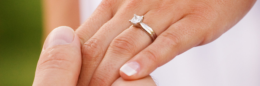 Uomo che stringe la mano di una donna con un anello di fidanzamento con diamante - BAUNAT