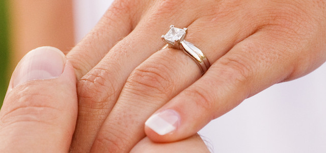 Uomo che stringe la mano di una donna con un anello di fidanzamento con diamante - BAUNAT