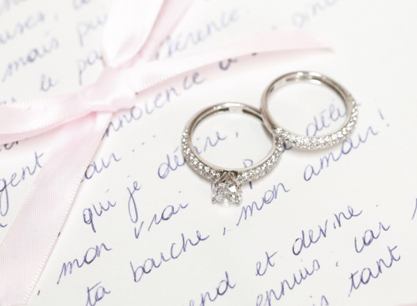 Fede nuziale e anello di fidanzamento appoggiati su una lettera, splendidamente legati con un nastro rosa, simbolo di amore e impegno.