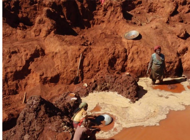 persone che cercano oro in una zona fangosa, utilizzando secchi per setacciare le rive del fiume alla ricerca di reperti preziosi