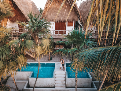 Una coppia in piedi a bordo piscina, circondata da palme lussureggianti, si gode una giornata di sole in un paradiso tropicale. 
