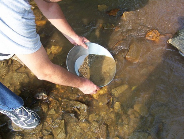 Un uomo usa una ciotola di metallo nell'acqua, praticando il metodo della ricerca dell'oro per trovare pepite preziose.