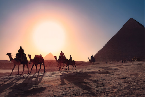 The sun dips below the Giza pyramids, painting the sky with vibrant colours in this iconic scene of ancient Egypt.