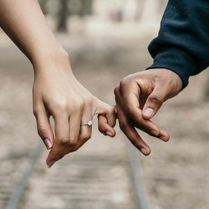A close-up of a man and a woman holding pinkies. The woman is wearing a simple diamond promise ring.
