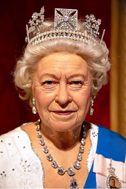 A portrait of the late Queen Elizabeth II wearing a pearl and diamond crown, a necklace of large diamonds and a pin of her late husband.