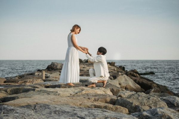a man bending the knee for his fiancé at the beach, asking her to get married
