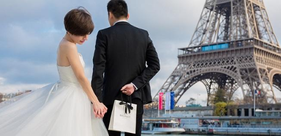 man about to propose in public in front of the Eiffel Tower holding a BAUNAT bag with a diamond engagement ring